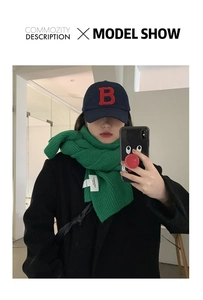 Detail of thick green knit scarf paired with navy baseball cap and black wool coat