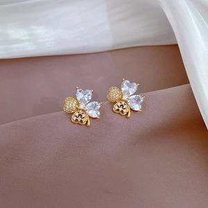Macro shot of gold clover stud earrings with heart-shaped crystals and zircon