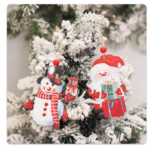 Close-up of wooden Santa and Snowman ornaments hanging on snow-covered pine branches