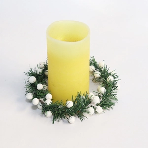 Close-up of yellow pillar candle with green pine needles and white berry wreath base