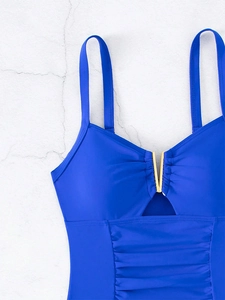 Detail of royal blue swimsuit with gold V-hardware, cutout design, and ruched belly fabric