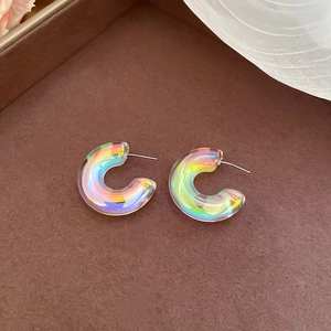 Macro shot of iridescent acrylic C-shape hoop earrings with silver pins on brown base