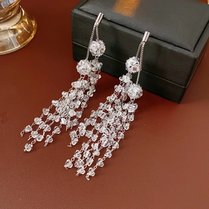 Close-up of silver crystal tassel earrings displayed on premium brown leather texture