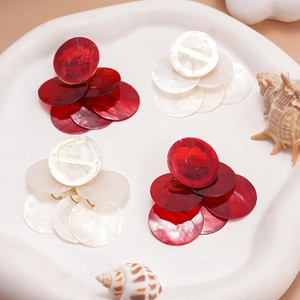 Close-up of layered shell-textured round earrings in red and white on a tray