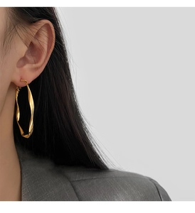 Close-up of a model wearing large twisted gold hoop earrings with a minimalist style