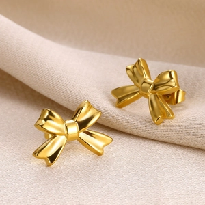 Detailed close-up of polished 18K gold-plated bow stud earrings on textured fabric