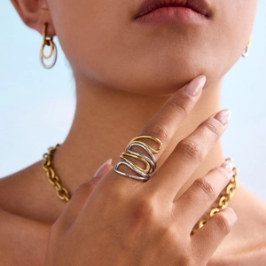 Minimalist bicolor wave ring and gold chain jewelry set shown on a model against blue background