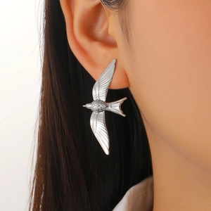 Macro detail of silver stainless steel bird earring showing intricate feather textures on ear