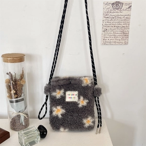 Detail of grey plush crossbody bag with daisy embroidery and a black and white cord strap