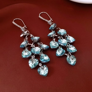 Detailed shot of cascading heart-shaped blue crystals and fringed silver tassel earrings