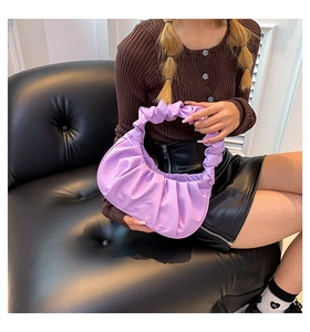 Detailed view of a purple ruched crescent handbag held by a model on a leather sofa