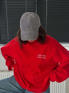 Red crewneck sweatshirt with white letter embroidery paired with a grey corduroy cap