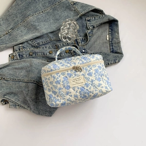 Detailed close-up of blue floral quilted cosmetic bag next to denim jacket on white background