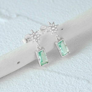 Macro shot of S925 silver star earrings with emerald-cut green gemstone and white zircons