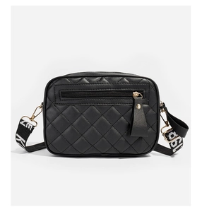 Close-up of black quilted camera bag with gold zipper and patterned woven strap