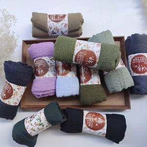 Detailed texture of pleated cotton scarves in multiple colors on a rustic wooden tray