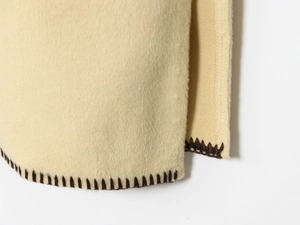 Close-up of cream textile jacket edge with contrast dark brown blanket stitching detail