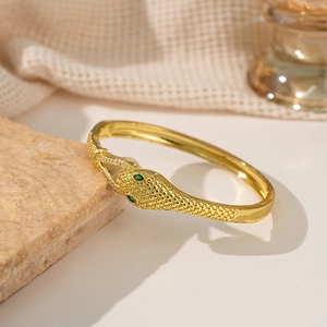 Goldenes Schlangenarmband mit grünen Steinaugen und weißen Zirkonia auf Steinuntergrund