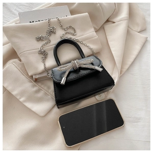 Detail of a mini black crossbody bag with silver rhinestone bow on a beige blazer
