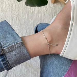 Close-up of minimalist 925 sterling silver beaded anklet with long bar pendant on ankle