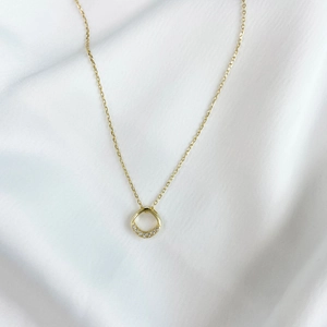 Detail of a minimalist 14k gold-plated square necklace on white silk fabric background