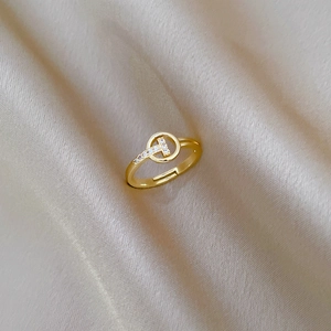 Macro detail of golden T-letter ring with sparkling zircons on elegant champagne silk fabric