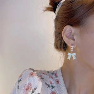 Close-up of model wearing white bow long earrings with elegant pearl drop details