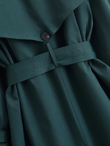 Macro detail of dark green trench coat showing twill fabric texture and button closure