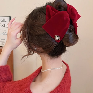 Détail d'une pince à cheveux en velours rouge avec camélia et perle sur une coiffure chic