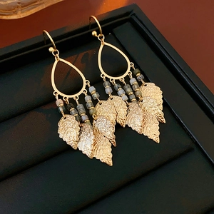 Détail de boucles d'oreilles feuilles dorées avec cadre en goutte et petites perles