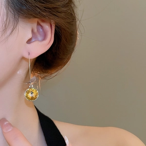 Detail view of round faceted yellow gemstone earring on model with silver hook