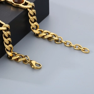 Macro detail of gold Cuban chain bracelet with lobster clasp and amber gemstone inlay