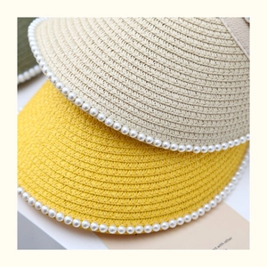 Close-up of straw sun visors with pearl trim detailing in yellow and beige colors
