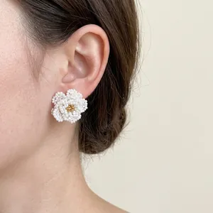Elegant beaded camellia flower stud earrings with gold center worn by a model