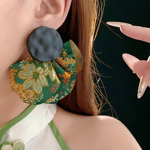 Close-up of fan-shaped green brocade earring with golden patterns on a model