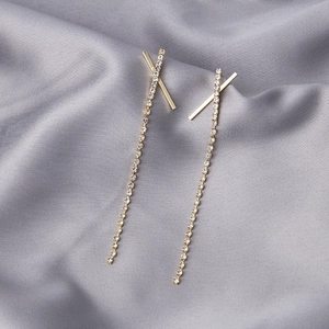 Close-up of golden tassel earrings with sparkling rhinestones on grey silk background