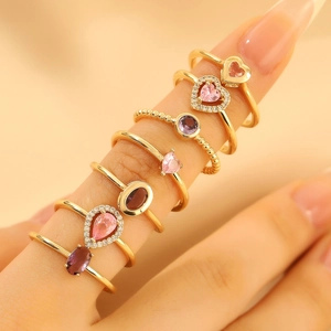 Golden rings set with pink and purple heart stones worn on fingers in warm light
