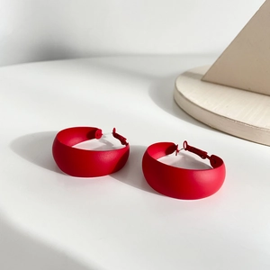 Detail view of bold red C-shaped hoop earrings with a matte finish on a white surface