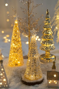 Close-up of glowing glass Christmas trees with warm LED light and textured gold finish