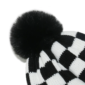 Detail of checkered knit beanie with a fluffy faux fur pompom on top for winter