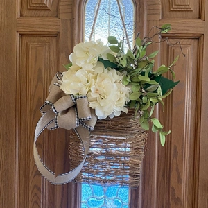 Detail of white artificial hydrangea basket with burlap bow hanging on a wooden door