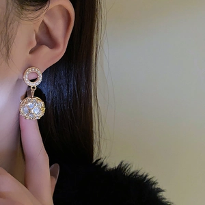 Close-up of golden pearl earrings with hollow spherical charms worn by a model