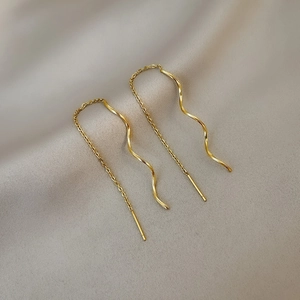 Detail view of golden wave threader earrings on a textured grey fabric background