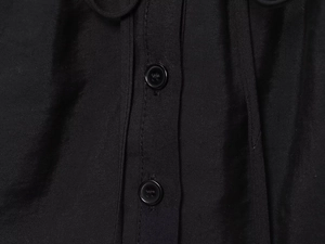 Gros plan sur la texture en sergé noir et les boutons en résine d'un caraco fluide chic