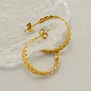 Golden hollow geometric hoop earrings on textured glass plate, stainless steel jewelry