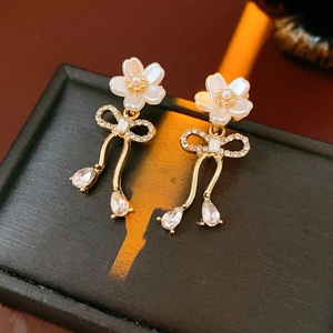 Gros plan de boucles d'oreilles fleuries dorées avec perles et nœuds en diamant sur écrin