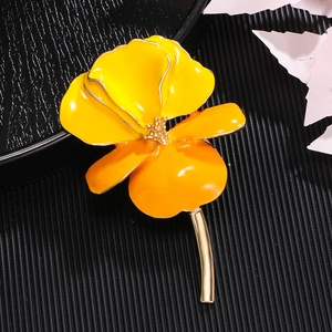 Vintage enamel iris flower brooch in yellow and orange on a textured black surface