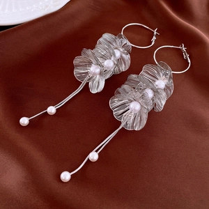 Macro detail of silver floral tassel earrings with pearls on dark brown satin fabric