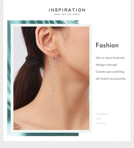 Detail of long silver tassel earring with beads worn by a model on light background