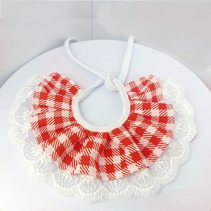 Detailed view of red plaid pet bib with white lace edges on a minimalist tray